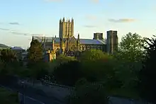 Stone building seen above surrounding trees. There are three towers the central one is more ornate and higher than the other two