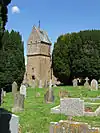 Building with square tower. In the foreground are gravestones.