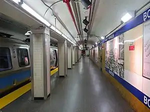 A subway train at an underground platform with blue signage