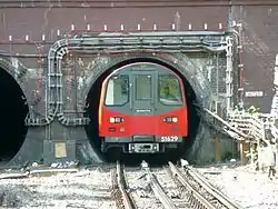 A London Underground deep-level tube train emerging from a tunnel. Attempting to ride on the side or on the roof of underground metro trains is especially dangerous due to the very small clearance between the train and the tunnel wall on many systems.