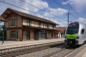 Silver-and-green train passes two-story building with gabled roof