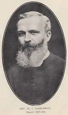 Oval portrait photo of Carr Smith, a strong-faced man with large square forehead, deep-set dark eyes, and a bristly beard partly grey and partly white.