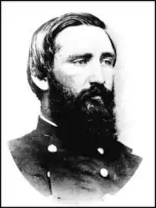 Black and white photo shows a bearded man with neatly combed hair wearing a dark military uniform.