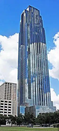 Tall, symmetrical,  glass skyscraper with triangular peak, and setbacks that narrow the building as it rises.  A chevron design under the top seems to be pushed upward by  a long, thin arrow.