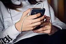 Adolescents holding a smartphone device, with plugged in ear buds.