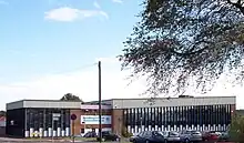 A building approximately 3 stories high. For the most part, the building is made up of horizontal columns of an opaque white panel up to around head height, with 3 windows arranged vertically above this. The columns are approximately 0.5 m (1.6 ft) wide and run from just below the roof to just above ground level and are separated by vertical wooden beams. Above the columns of windows a corrugated white border runs along the top of the building.