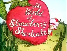 A 6-year-old girl, dressed in a pinafore and wearing a pink dust cap on top of her hair, looks out to the right of a giant strawberry. On the strawberry, the words "The World of Strawberry Shortcake" are written in cursive.