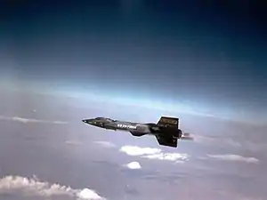 Black rocket aircraft with stubby wings and short vertical stabilizers above and below tail unit