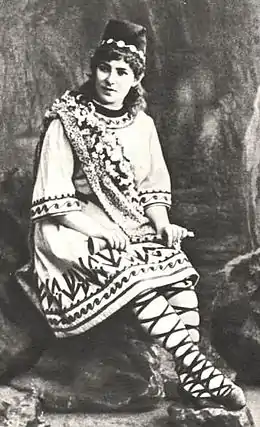 A white woman, seated, in theatrical costume