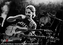 Yossi Sassi sitting on a stage, playing a double-necked stringed instrument