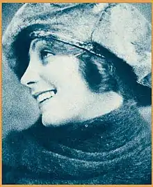 A smiling young woman wearing a cloth cap low over her brow, in profile