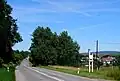 Main road next to the village and village welcome sign (August 2011)