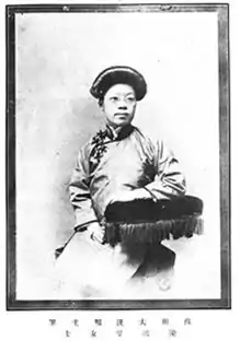 Zhang Mojun, wearing glasses, in a studio portrait photograph. She is wearing Chinese clothing and leaning on a cushion.