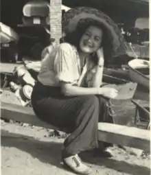 A young Dr. Vázquez sitting on a wooden plank smiling and holding her glasses