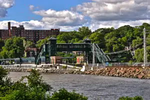 Green train station overpass by a river and brick apartment building