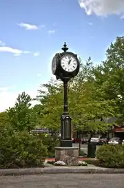 A large four-faced clock in front of shops