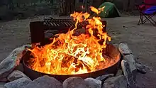 A campfire inside a metal container, surrounded by rocks and bare dirt