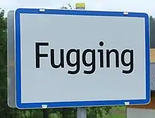 A road sign for the town of Fugging. The sign simply says "Fugging", and has a blue rectangular border around a white background, with the black text of the town name.