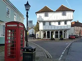 A red telephone box in front of an ancient wooden building, painted in white.