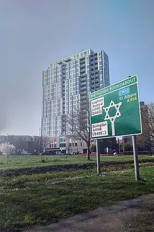 A modern building appears behind a complicated-looking sign - a series of mini roundabouts arranged in a loop on a green A-road sign, with branches going off in several directions.