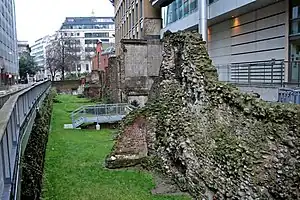 Photograph of ruins of the London Wall between a street and office buildings.