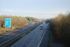 The M11 on the outskirts of Cambridge, with a blue sign for Ely and Huntingdon as an HGV speeds towards the photographer on a two-lane dual-carriageway