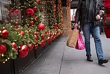 A man carries shopping bags past red and green Christmas decorations