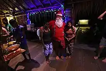 A man dressed as Santa hugging two women in a small night club